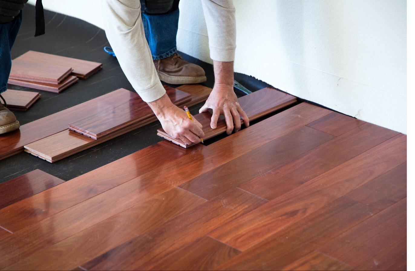 Skilled craftsman installing hardwood flooring planks with precision marking — ten years of installation experience at Siddhi Decorators, Pitampura